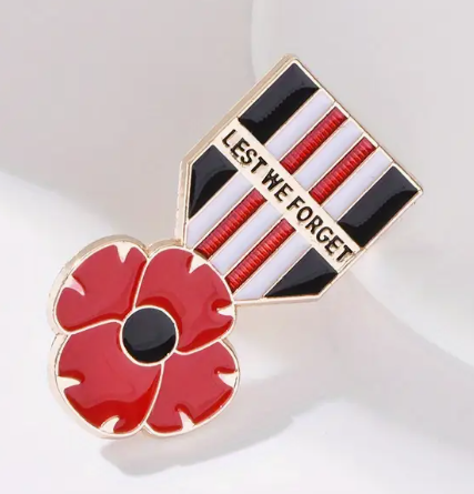 Pin with red poppy flower and 'Lest We Forget' ribbon on a white background